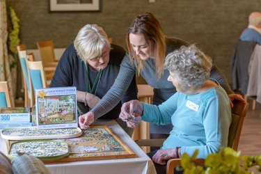 Two young people help an elderly person with a puzzle.