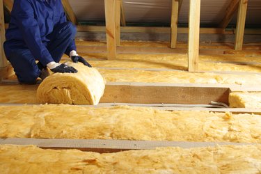 Worker thermally insulating house attic with glass wool