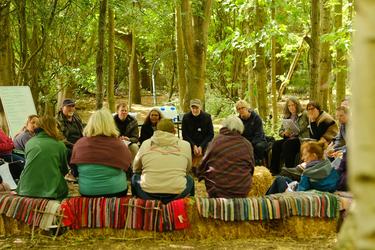 A group of people sit in a circle in the woods at a nature event.