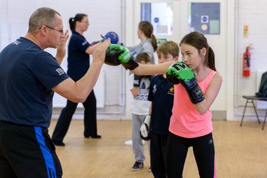 Two children and an instructor practice boxing at a club.